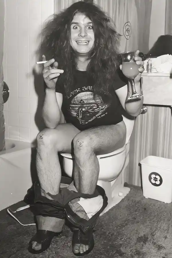 The late Ozzy Osbourne, smoking and drinking while sitting on a toilet. With his pants down, od course.
